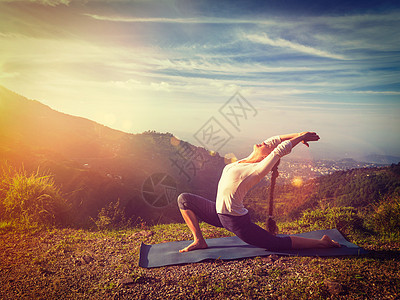 户外瑜伽运动健康的女人练瑜伽安贾尼雅萨纳低月牙弓步姿势户外山区早上光泄漏镜头耀斑复古效果过滤时尚风格的形象图片