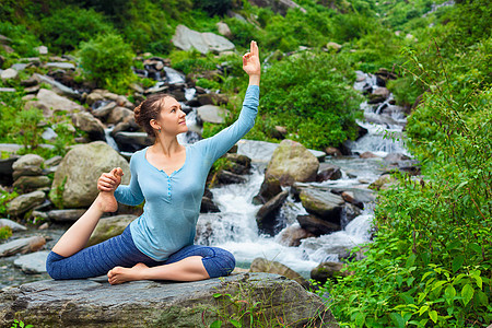 哈他瑜伽户外轻运动健康的女人瑜伽阿莎娜EkaPadaRajakapotasana条腿的鸽子姿势热带瀑布印度希马查图片