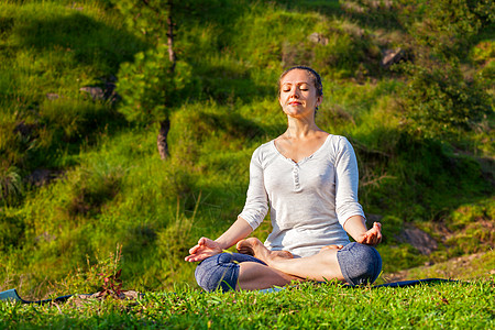 轻运动健康的女人户外瑜伽冥想放松帕德马萨纳莲花姿势与下巴泥德拉绿色的草地森林轻的运动健康的女人瑜伽莲花图片