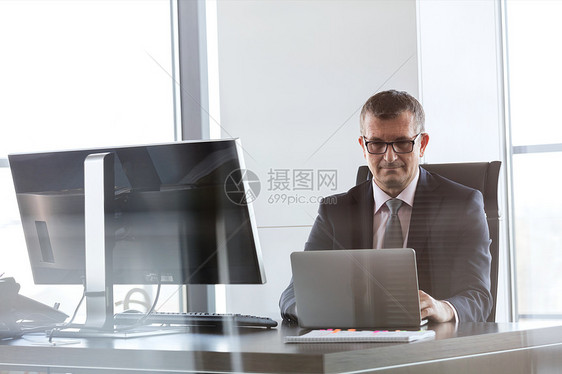 自信成熟的商人办公室的桌子上用笔记本电脑图片