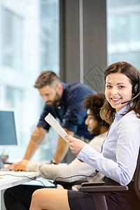 微笑的女客户服务代表的肖像,与同事办公室的背景图片