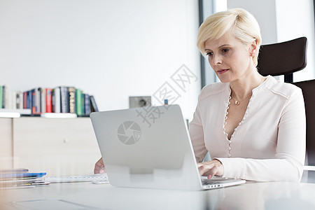 成熟的女商人办公室的桌子上用笔记本电脑图片