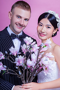 微笑的新婚夫妇粉红色背景下着人造花的肖像图片