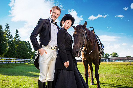 自信的穿着得体的夫妇站田野上马的肖像图片