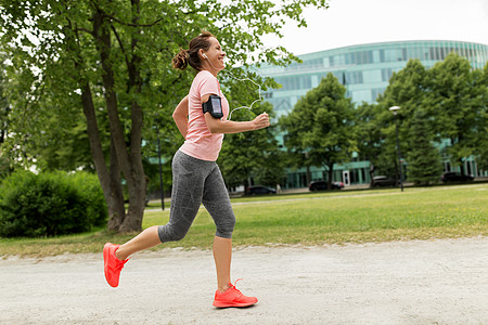 健身,运动健康的生活方式微笑的女人戴着带智能手机的,公园慢跑听音乐带耳机的女人公园里增加慢跑图片