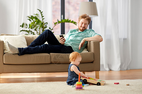 家庭,父亲人的快乐的红头发父亲与智能手机小宝贝女儿玩玩具积木套件家里爸爸宝宝家玩玩具积木图片