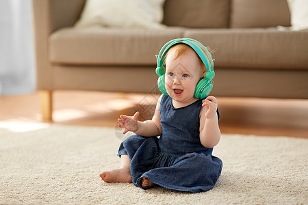 童享好音乐童,孩子技术可爱的红头发女孩耳机听音乐家红头发的女婴戴着耳机听音乐背景