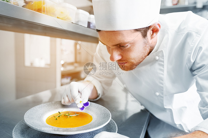 食物烹饪,职业人的快乐的男厨师烹饪服务装饰盘子的汤与花餐厅厨房快乐的男厨师餐厅厨房烹饪食物图片