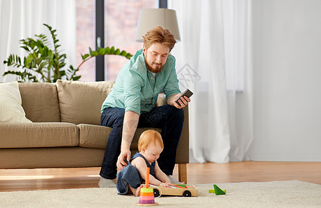 家庭,父亲人的快乐的红头发父亲与智能手机小宝贝女儿玩玩具积木套件家里爸爸宝宝家玩玩具积木图片