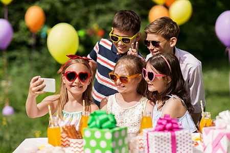 假期,童技术快乐的孩子戴着太阳镜,夏季花园的生日聚会上用智能手机自拍快乐的孩子生日聚会上自拍图片