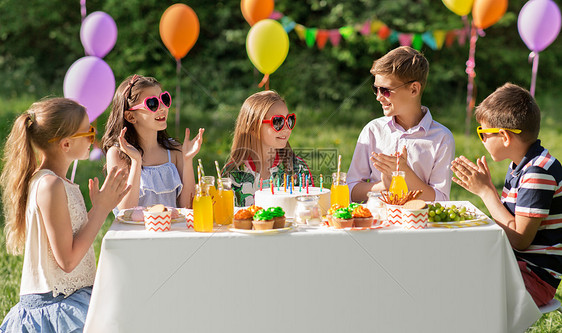 假期,童庆祝快乐的孩子蛋糕上着蜡烛,坐夏天的花园聚会上,为生日女孩鼓掌快乐的孩子夏天的生日聚会上吃蛋糕图片