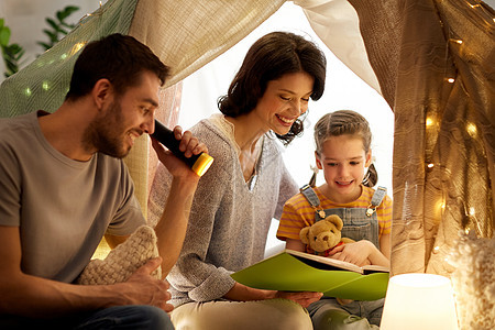 家庭,潮格人的快乐的母亲,父亲小女儿阅读书与火炬灯孩子们的帐篷晚上家孩子们家帐篷里快乐的家庭读物图片