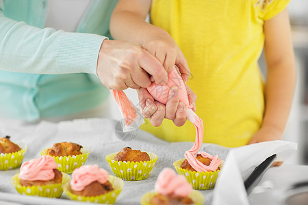 家庭,烹饪人的母亲小女儿家庭厨房用奶油霜制作装饰纸杯蛋糕妈妈女儿家纸杯蛋糕图片