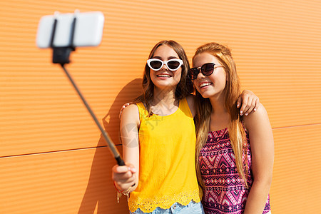 时尚休闲人的微笑的十几岁女孩夏天的户外自拍杆上用智能手机拍照十几岁的女孩用自拍杆拍照图片