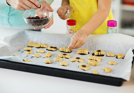 家庭,烹饪烘焙母亲小女儿用巧克力洒家庭厨房的托盘上装饰饼干母亲女儿家饼干图片