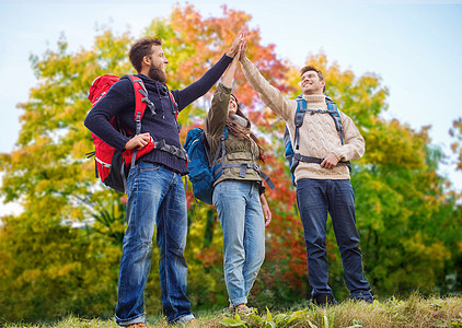 旅行,旅游,徒步旅行,手势人的群微笑的朋友,背包秋天的树背景下高出5朋友们秋天徒步旅行击掌图片