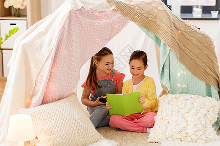 童,友谊潮湿的快乐的小女孩阅读书与火炬灯孩子帐篷帐篷家里小女孩家孩子们的帐篷里看书图片
