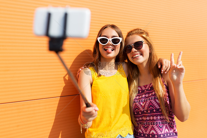 时尚,休闲人的微笑的十几岁女孩用智能手机自拍杆上拍照,并夏天户外展示平十几岁的女孩用自拍杆拍照图片