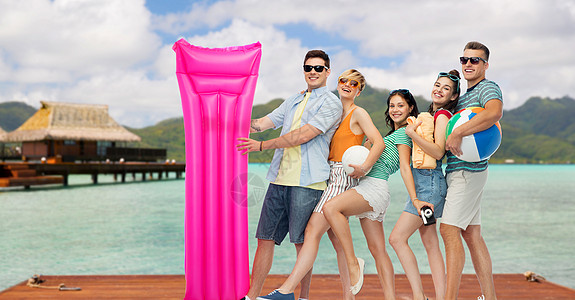 旅行,旅游暑假的群快乐的微笑朋友戴着太阳镜,带着沙滩球,排球,毛巾,相机漂浮的床垫波拉波拉的背景上快乐的朋友与图片