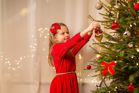 诞节,假日童的快乐的女孩穿着红色的衣服装饰自然冷杉树穿着红色连衣裙装饰诞树的快乐女孩图片