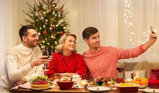 节日庆祝快乐的朋友家里的诞晚餐上用智能手机自拍朋友们诞晚餐上自拍图片