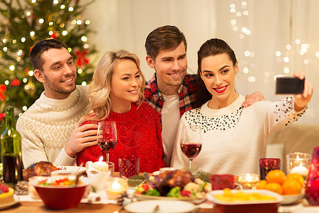 节日庆祝快乐的朋友家里的诞晚餐上用智能手机自拍朋友们诞晚餐上自拍图片