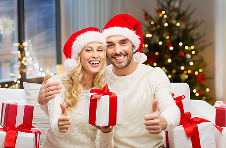 节日人们的幸福的夫妇戴着诞老人的帽子,礼品盒家里的诞树灯光背景上竖大拇指诞礼物竖大拇指的幸福夫妇图片