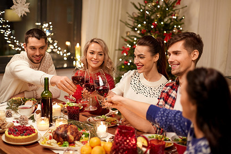 节日庆祝快乐的朋友家里吃诞晚餐,喝红酒碰杯朋友们庆祝诞节喝酒图片