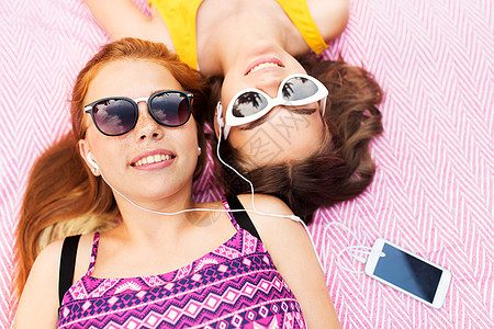 夏季时尚,休闲技术微笑的少女戴着太阳镜耳机躺野餐毯上,听着智能手机上的音乐十几岁的女孩智能手机听音乐图片
