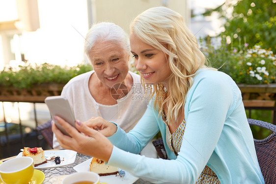 家庭,代人的快乐的微笑轻女儿长的母亲与智能手机咖啡馆餐厅露台女儿长的母亲咖啡馆着智能手机图片