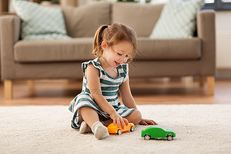 小孩玩具车童人的快乐的三岁女婴家里玩玩具车快乐的女婴家里玩玩具车背景