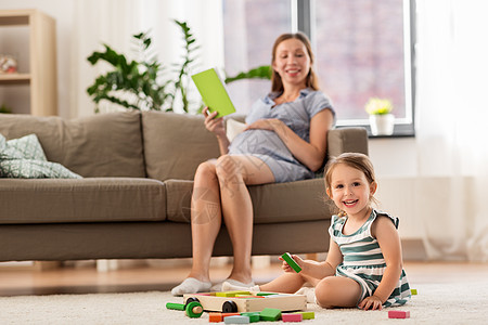 童人的快乐的三岁女婴玩玩具积木怀孕的母亲家看书快乐的女婴家里玩玩具积木图片