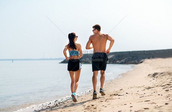 健身,运动生活方式的快乐的夫妇沿着夏天的海滩跑步穿着运动服的夫妇海滩上跑步图片