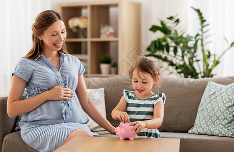 怀孕财务家庭观念快乐的怀孕母亲小女儿家里把欧元硬币放进储蓄罐里怀孕的母亲女儿带着储蓄罐图片
