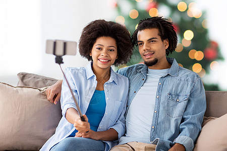 假日,技术人的快乐的非裔美国人夫妇与智能手机自拍家里的诞树灯光背景夫妇诞节用智能手机自拍图片