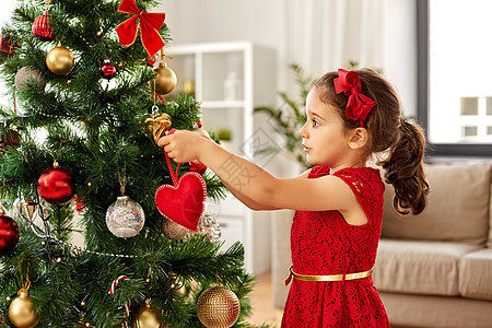 寒假,慈善人们的快乐的小女孩家里用红心玩具装饰诞树小女孩家装饰诞树背景图片