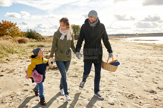 家庭休闲人的快乐的母亲,父亲小儿子沿着秋天的海滩散步,带着野餐篮毯子快乐的家人秋天海滩野餐图片