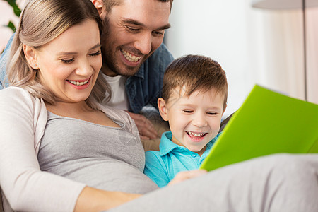 怀孕,人们家庭的快乐的怀孕母亲,父亲小儿子家沙发上看书家快乐的家庭读物图片