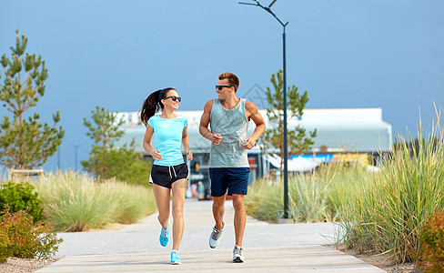 健身,运动生活方式的快乐的夫妇穿着运动服太阳镜沿着夏天的海滩小径跑步穿着运动服的夫妇沿着海滩小路跑步图片