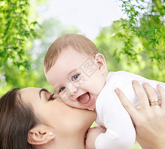 家庭母亲的快乐的微笑轻母亲亲吻小婴儿绿色的自然背景母亲绿色的自然背景下亲吻婴儿图片