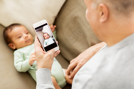 家庭父亲人的父亲家里用智能手机拍摄小儿子的特写父亲用智能手机给婴儿拍照图片