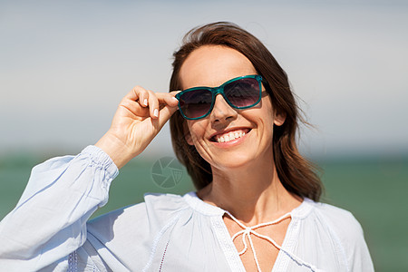 夏天,眼镜人的快乐的微笑女人戴着太阳镜海滩上夏天海滩上戴太阳镜的快乐微笑的女人图片