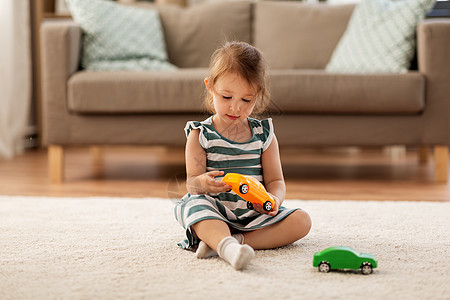 童人的快乐的三岁女婴家里玩玩具车快乐的女婴家里玩玩具车图片