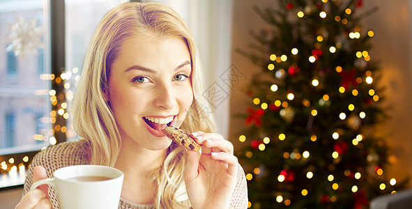 节日人们的快乐的轻女人家里用杯茶吃饼干,诞树的灯光背景上诞节家里喝茶吃饼干的女人图片