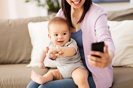 家庭母亲的快乐微笑的轻亚洲母亲与小婴儿儿子家里用智能手机自拍妈妈带着婴儿家自拍图片