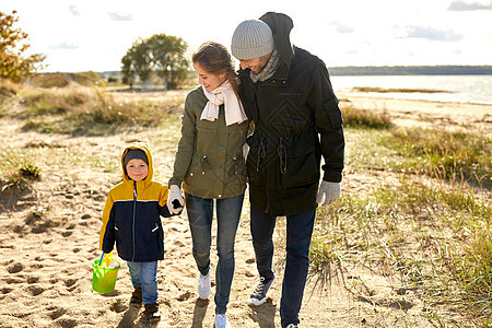 家庭,休闲人的快乐的母亲,父亲小儿子带着沙子玩具套件沿着秋天的海滩散步幸福的家庭沿着秋天的海滩散步图片