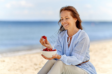 人们休闲的快乐的微笑的女人夏天的海滩上吃草莓快乐的女人夏天的海滩上吃草莓图片