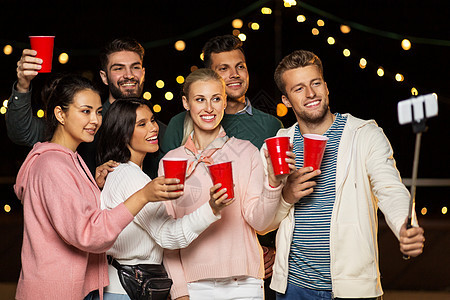休闲,庆祝人们的快乐的朋友与饮料拍照自拍杆屋顶聚会晚上饮料的朋友屋顶派上自拍图片