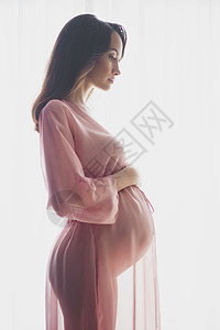 孕妇肚子穿着粉红色睡衣的美丽孕妇的生活方式肖像美好的早晨美丽健康背景