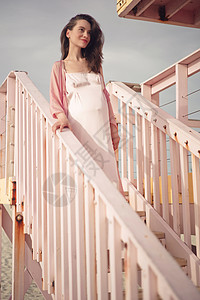 户外大气生活方式肖像美丽的孕妇穿着粉红色连衣裙粉红色救生员塔美好的早晨海滩上的日出美丽时尚粉红色的美学图片